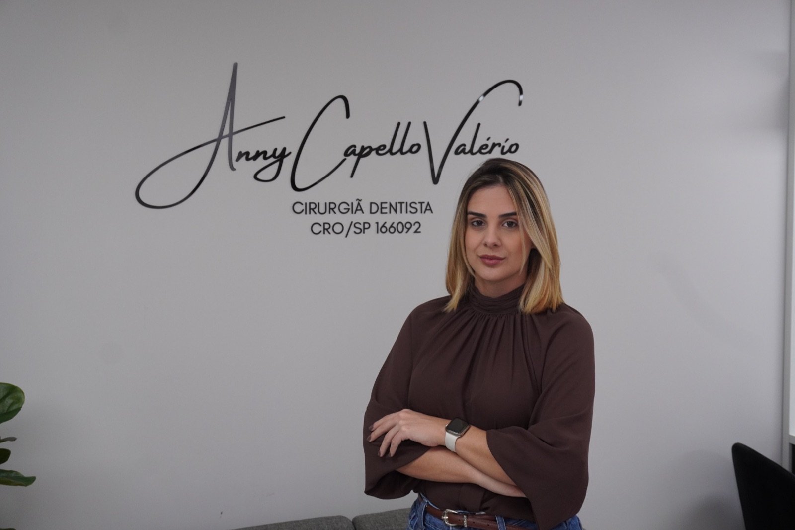 Dra. Anny Capello Valério no consultório, ao lado da identidade visual da clínica